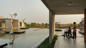 Exterior view of Bagchi Karunashraya Palliative Care Centre showing laterite stone architecture and natural landscaping.