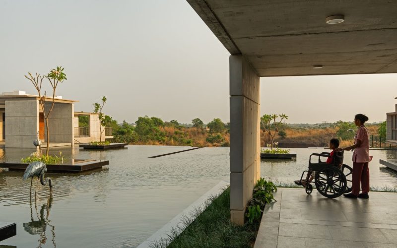 Exterior view of Bagchi Karunashraya Palliative Care Centre showing laterite stone architecture and natural landscaping.